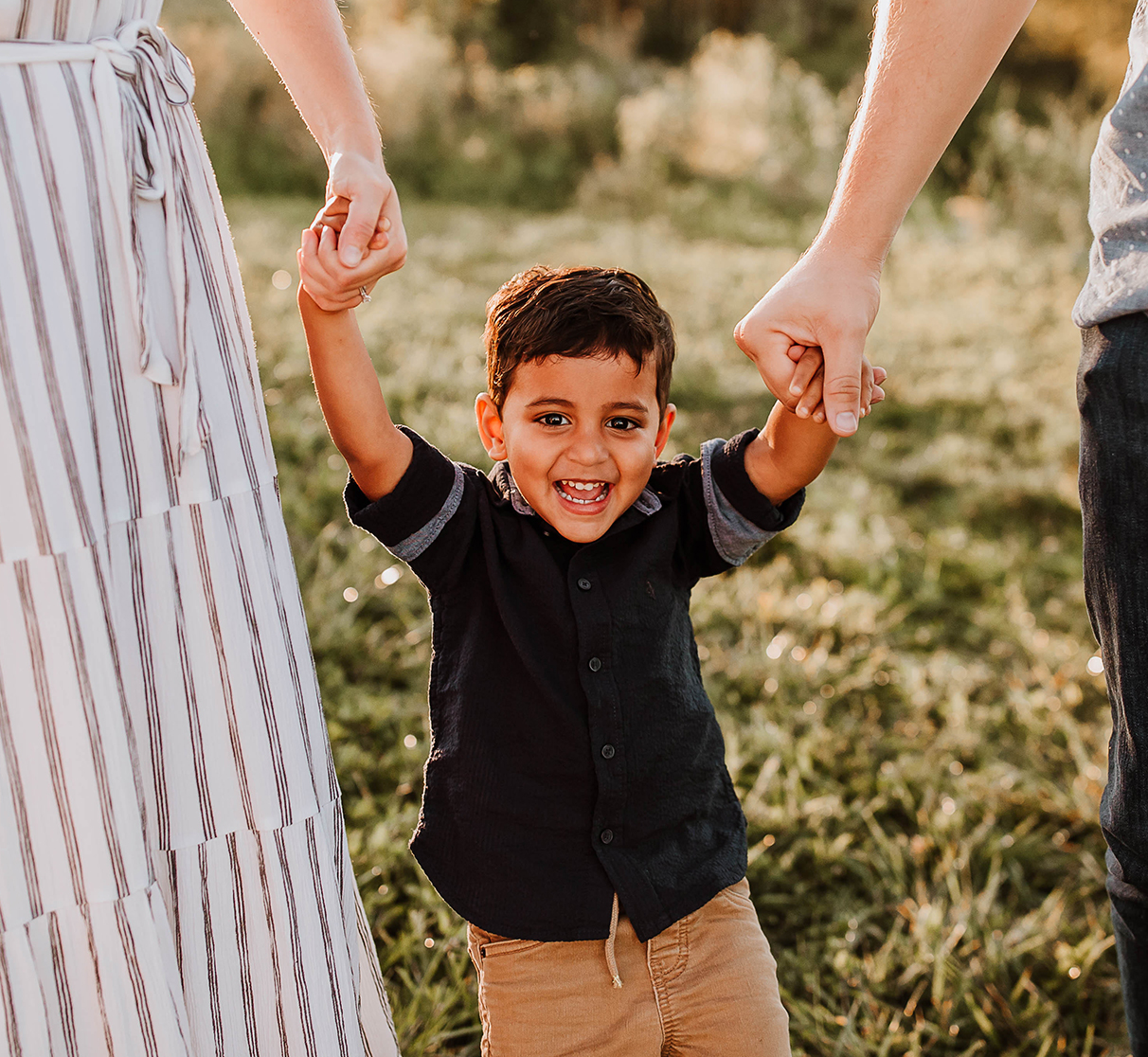 a little boy smiling and holding his parents hands